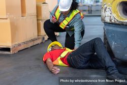 Black male in PPE gear passed out on warehouse floor with colleague offering help 0yo3O4