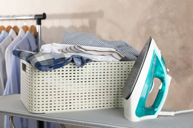 Basket with clean laundry and iron on ironing board, space for text
