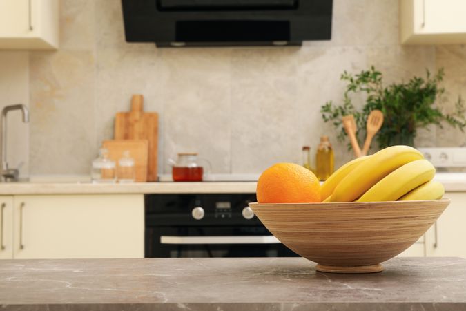 Bowl with fruits on gray table against kitchen interior