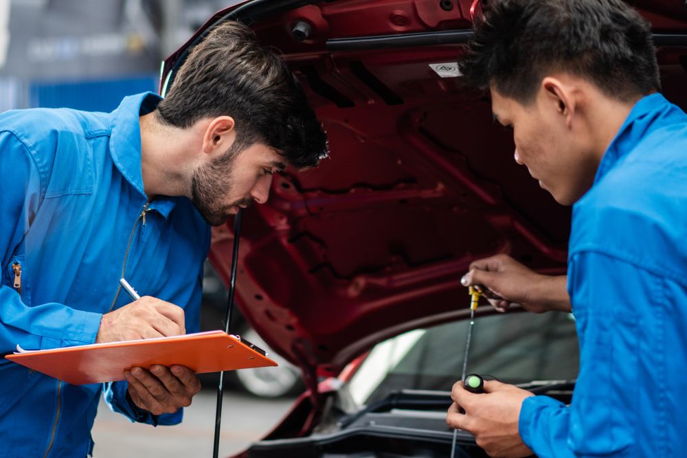 Two male auto workers standing working at open engine with clipboard