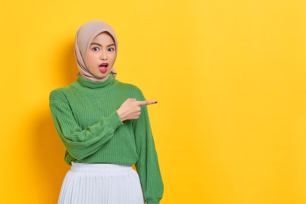 Surprised woman in headscarf pointing to the side