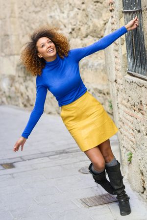 Joyful female with curly hair wearing bright blue shirt holding bars on window on street