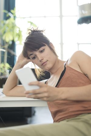 Woman looking at phone while leaning on desk