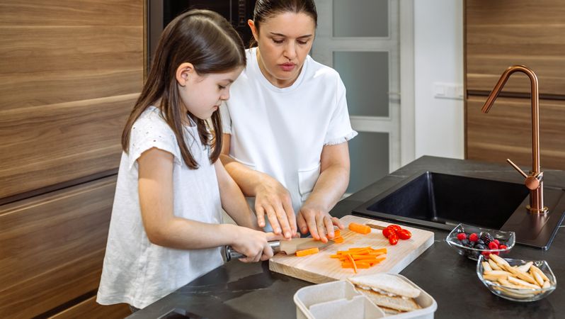 Mother teaching her daughter to cut vegetables for lunch box