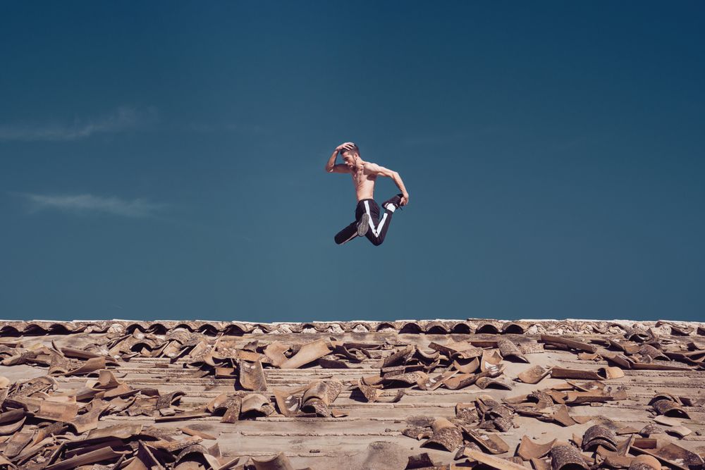 Strong active man jumping on roof while performing freestyle dance