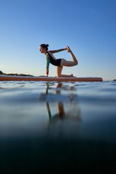 Female athlete in swimsuit taking Tiger pose on paddleboard at s