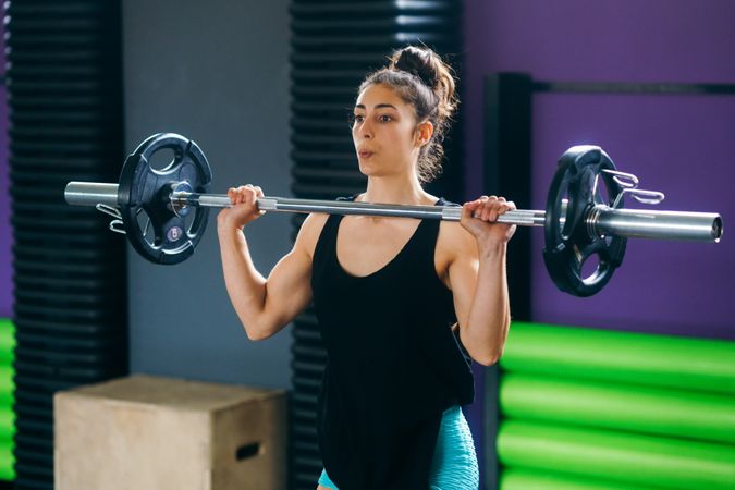Fit woman with barbell at her chest in gym