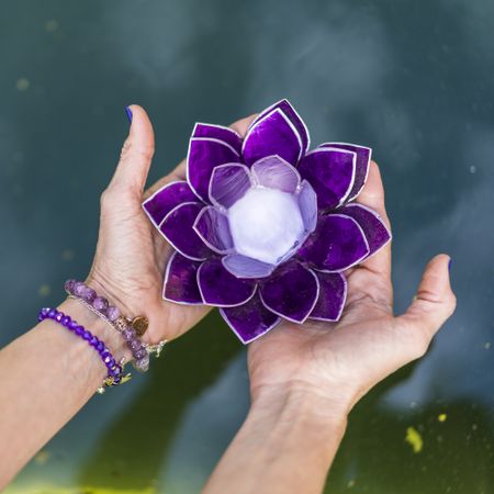 Top angle view of hands holding a purple glass lotus over water. Yoga and meditation concept.