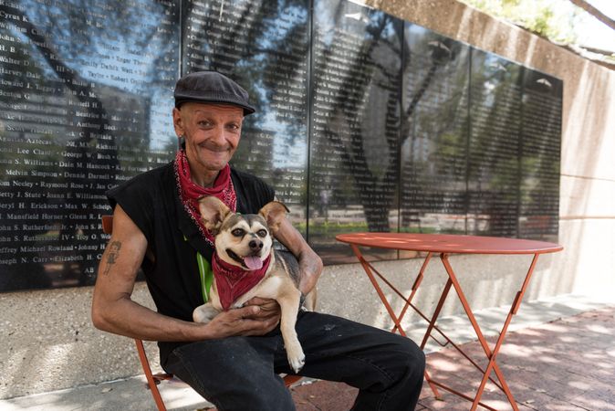 Man at red table smiling, with dog in matching red bandanas, Dallas, Texas