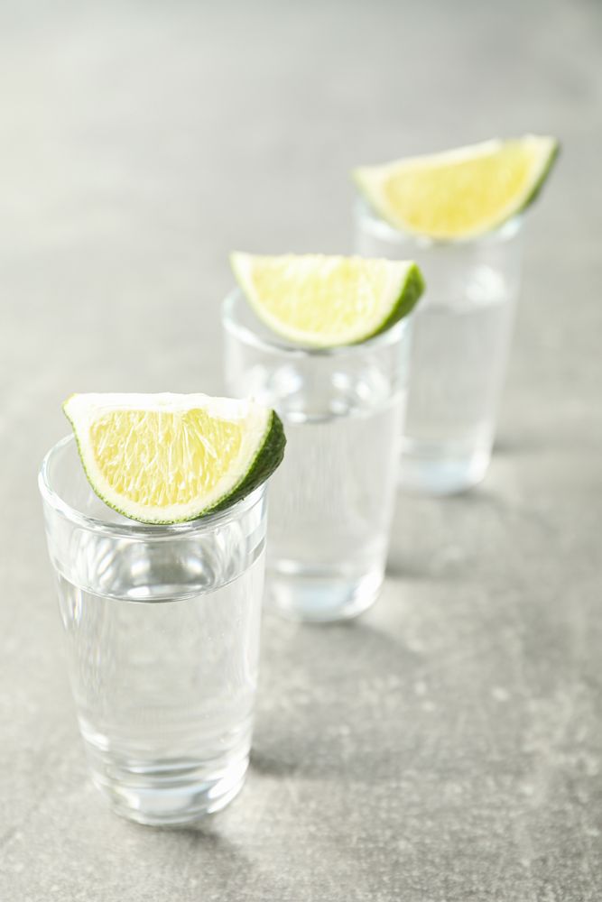 Tequila shots with lime slices on grey background