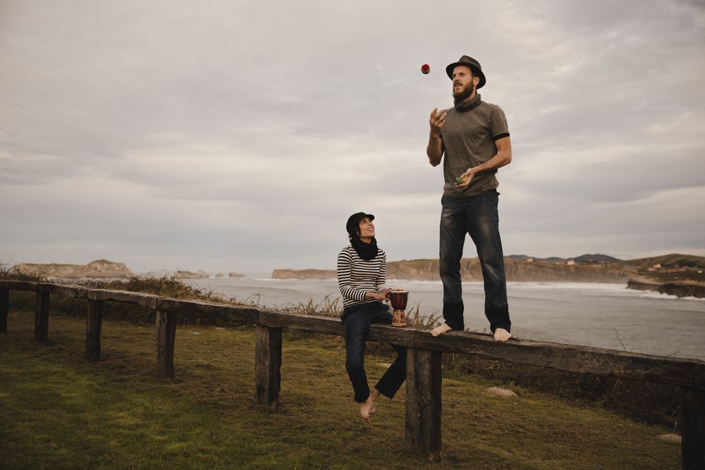 Man juggling balls on bench near woman with drum on shore