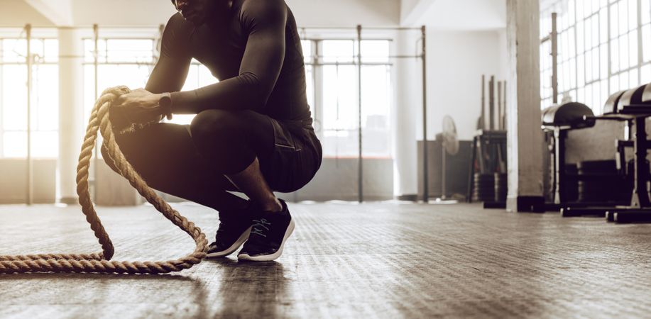 Cropped shot of man sitting on his toes holding a pair of battle ropes for workout