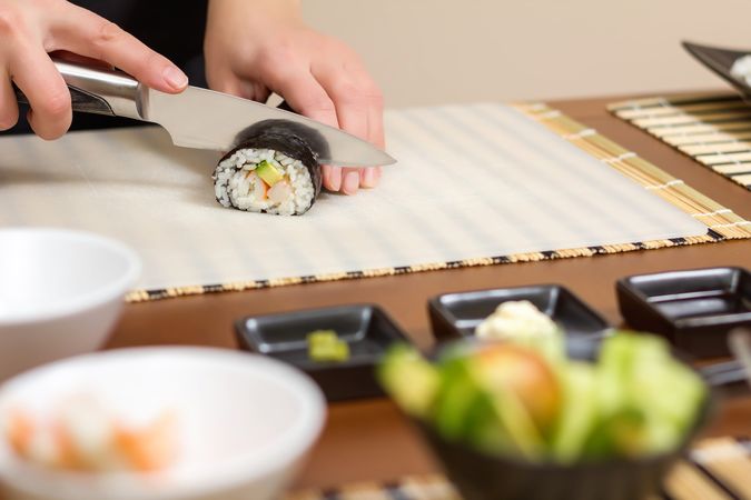 Female chef cutting Japanese sushi rolls with filling in nori seaweed sheet, copy space