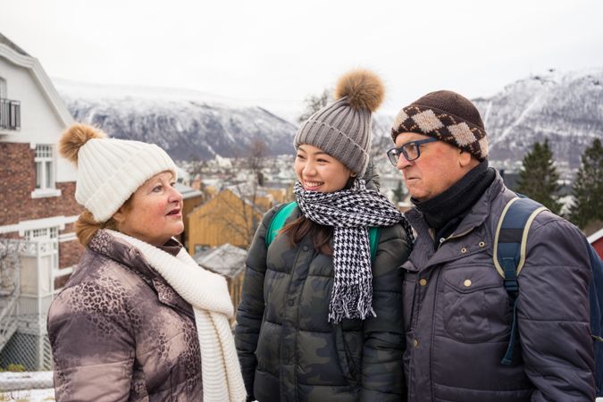 Asian resting female in warm clothing smiling while communicating with locals man and woman at city street