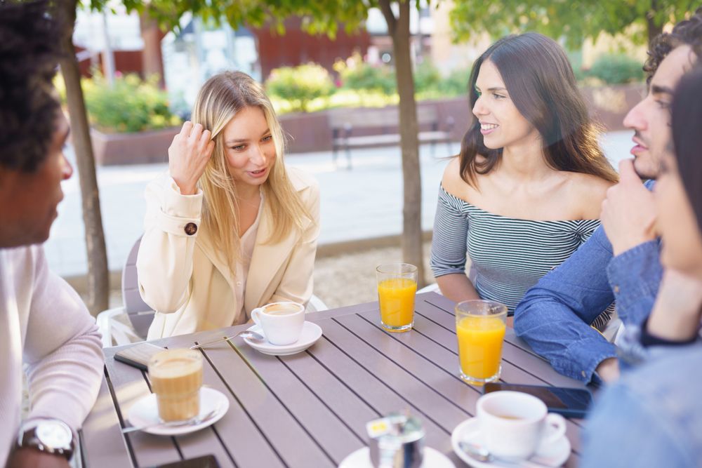 Multi-ethnic friends having a conversation over coffee and juice at outside table
