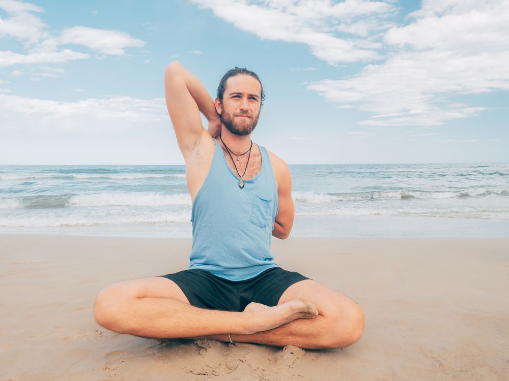 Man training yoga on beach
