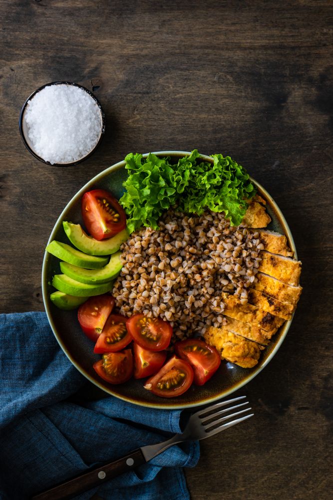 Healthy bowl of dinner with buckwheat, lettuce, avocado, and meat on wooden table