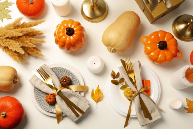 Golden cutlery on plates and pumpkins on light background, top view