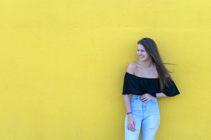 Smiling woman leaning on yellow wall on a sunny day