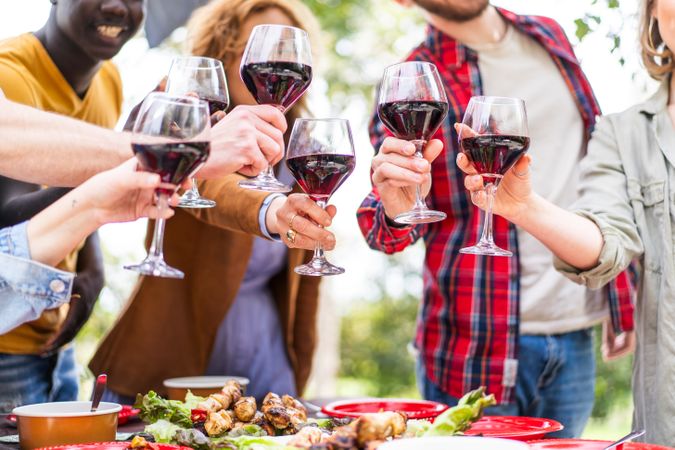 Close-up of a toast with red wine glasses over a meal on an outdoor table
