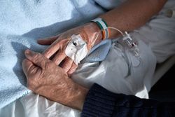 Crop anonymous mature male holding hand of sick wife in clinic