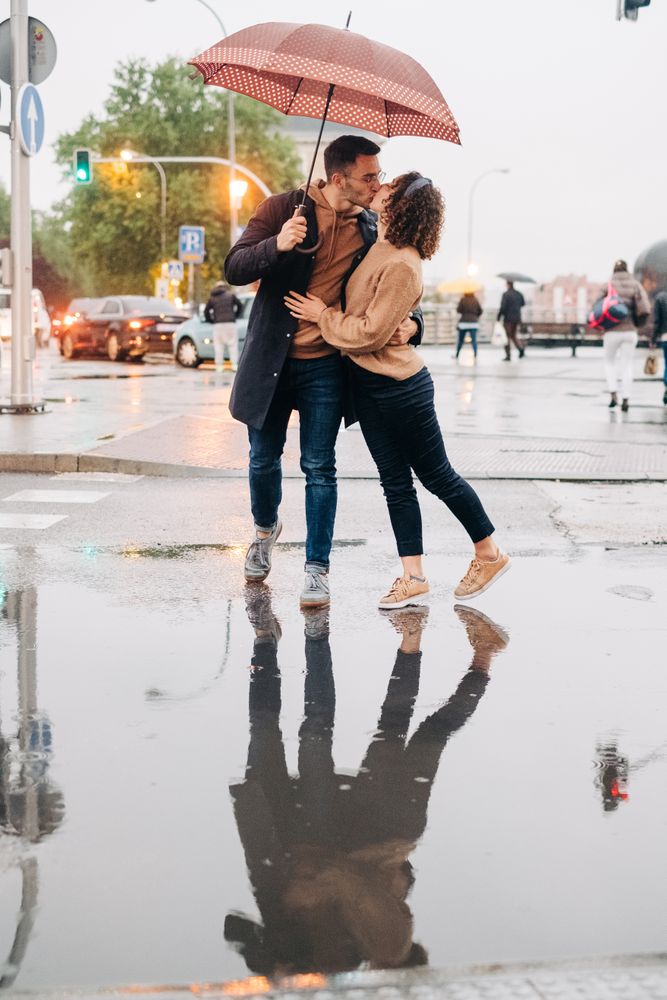 Happy couple with umbrella hugging on wet street