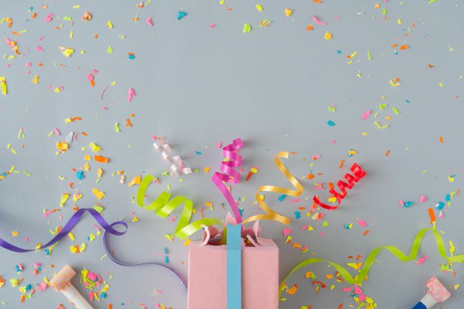 Present with confetti and colorful streamings on grey background