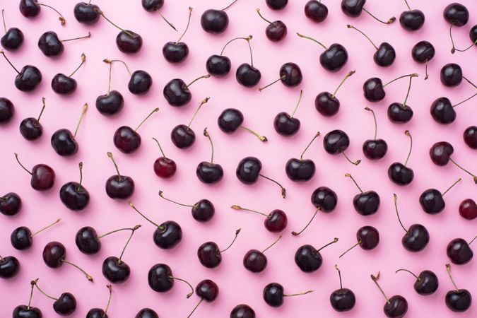 Many cherries scattered over a pink background