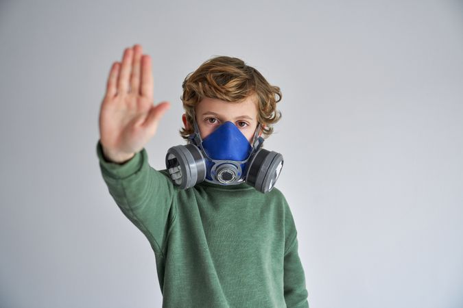 Calm child in respirator showing keep distance gesture in gray s