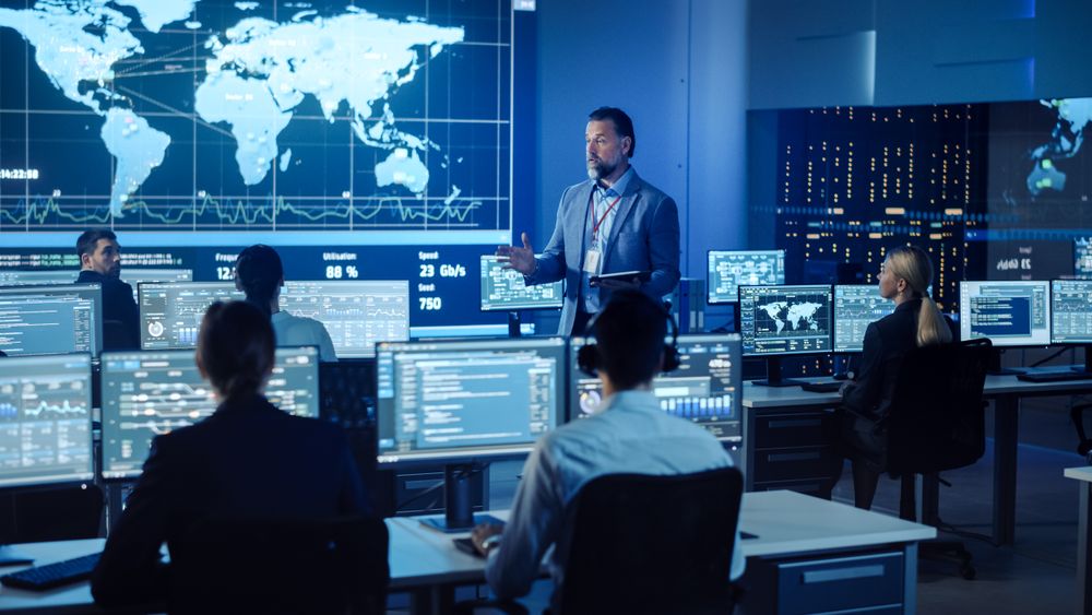 Bearded Executive Presents to Team in High-tech Command Center.