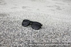 Sunglasses sitting on grey sandy beach bD99p0