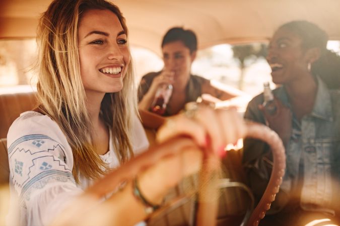 Beautiful young woman driving a car with friends having drink