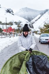 Smiling woman folding tent in countryside at winter