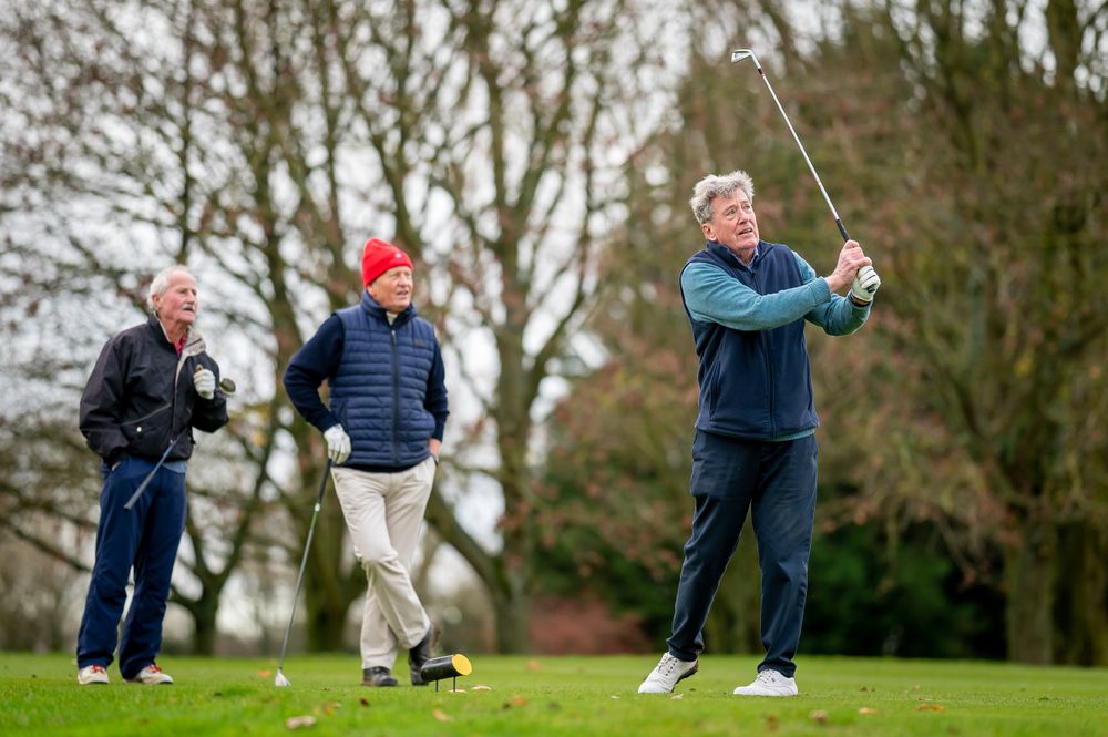 Man swinging on golf course with friends looking on