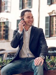 Smiling well dressed male having phone conversation on bench