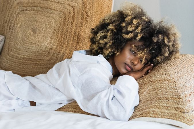 Thoughtful Black woman lying on bed in bedroom