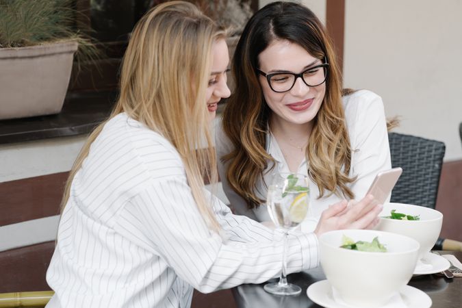 Women friends using smartphone at restaurant table