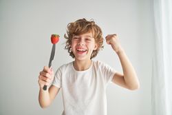 Positive boy with strawberry on top of knife