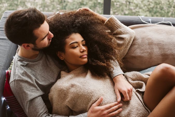 Young multiracial couple hugging on sofa