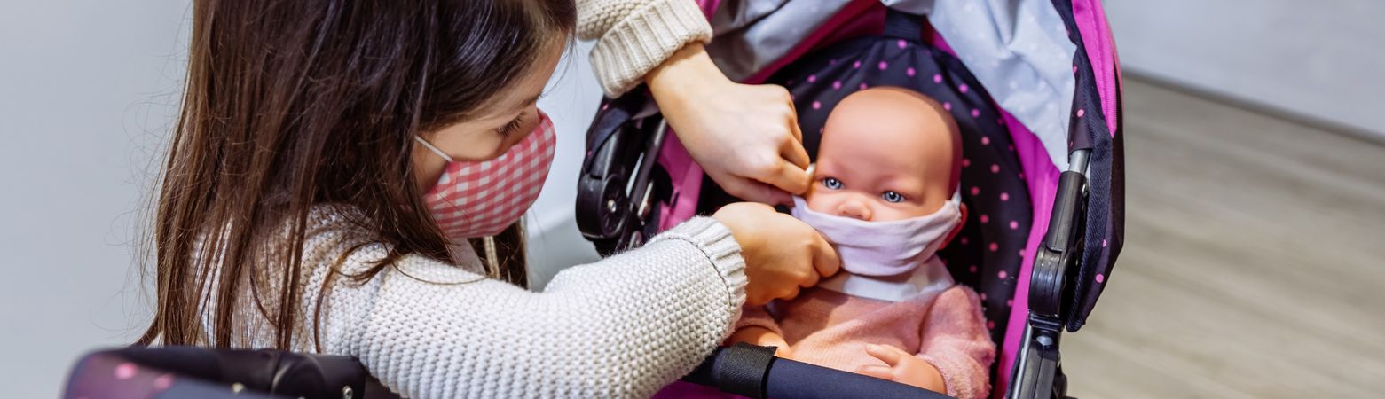 Girl with face mask putting mask on her baby doll