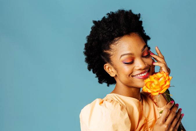 Studio shot of a smiling Black woman holding a yellow rose with her hand to her temple