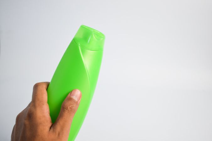Hand holding green shampoo bottle with no labels