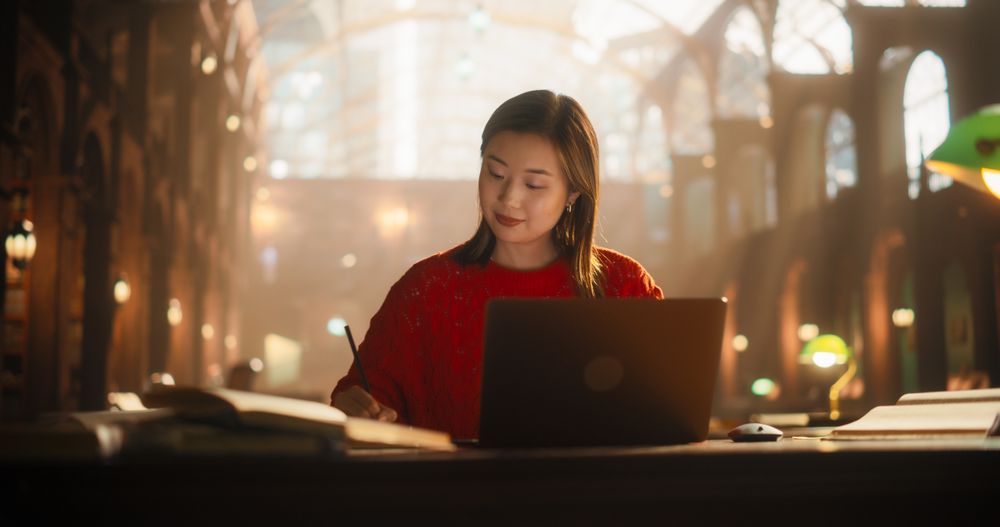 Diligent Asian Female Student Engaged in E-Learning with a Laptop and Books in a Classical Library