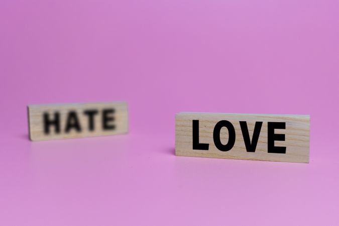 focus love word and blur hate word on wooden blocks isolated on pink background