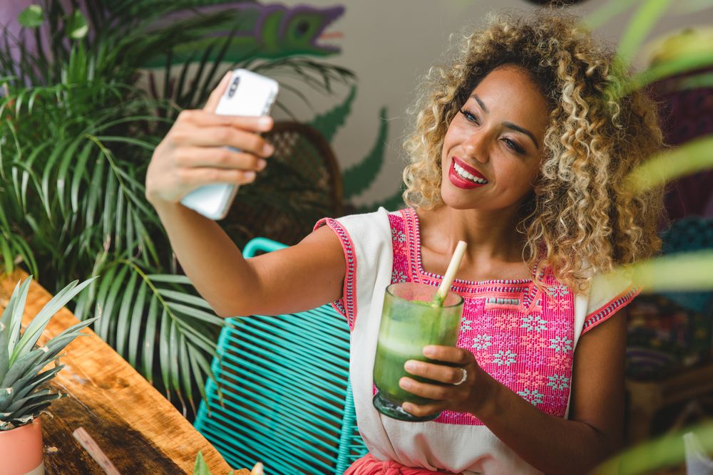 Black woman with fresh shake taking selfie on smartphone
