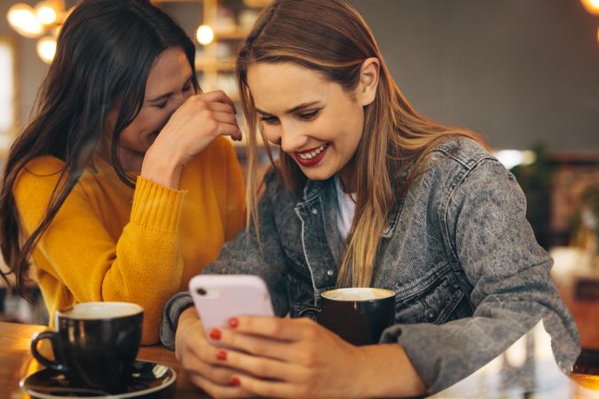 Woman showing something funny on her mobile phone to her friend and smiling