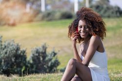 Female in light summer dress sitting in park speaking on her phone