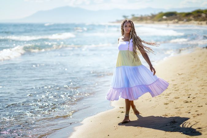 Carefree Black female walking along the shore in colorful dress