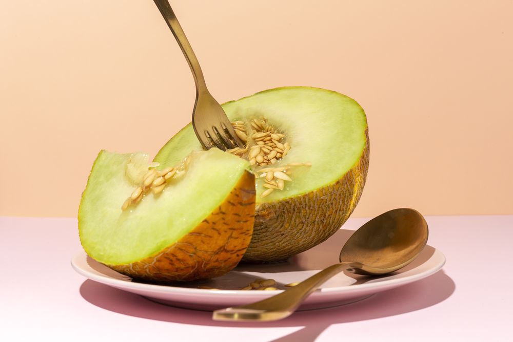 Sliced small melon on plate with spoon and fork