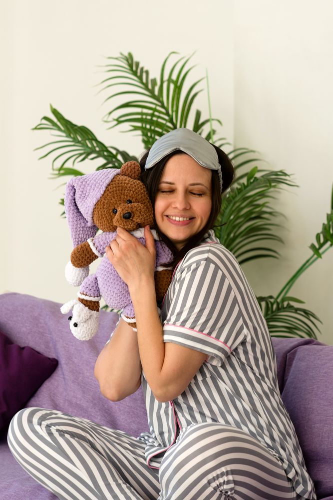Woman in striped pajamas hugs plush bear, smiling warmly.